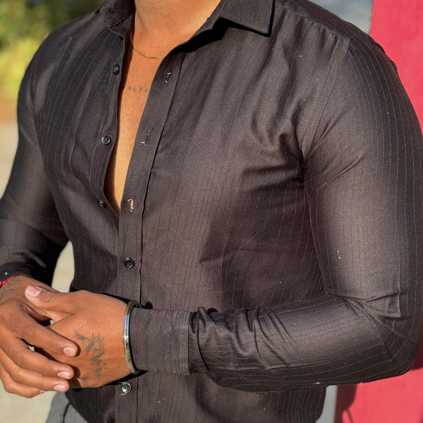 Man wearing a black dress shirt with rolled-up sleeves, standing against a blurred background.